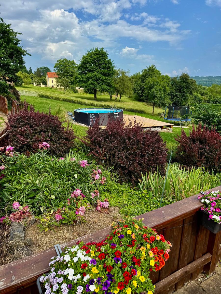 Kvetoucí truhlíky, za nimi zahrada s bazénem a krajina